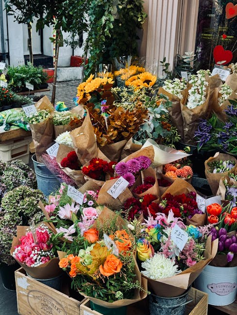 A vibrant display of freshly arranged flower bouquets outside a flower shop, featuring a variety of blooms including bright yellow sunflowers, pink lilies, red roses, purple irises, and white chrysant